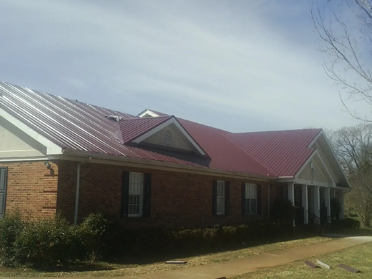 Red metal roof with gabled entries on a long brick building, from a Hail Damage Roof Repair job in Nunda