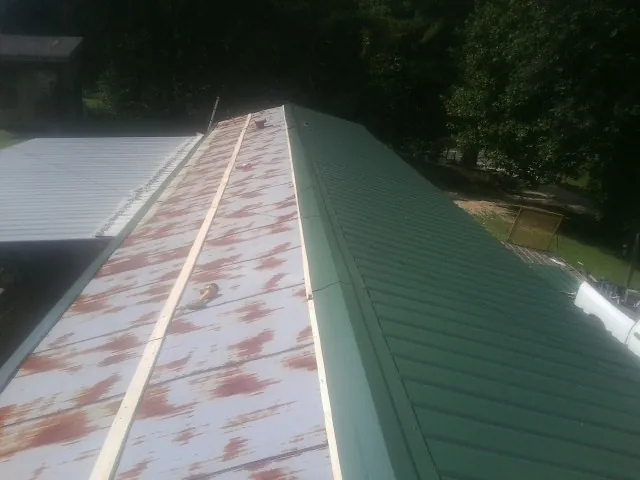Old rusted panels beside newly installed green metal roofing — Wind Damage Roof Repair by Roofing Brothers in Nunda